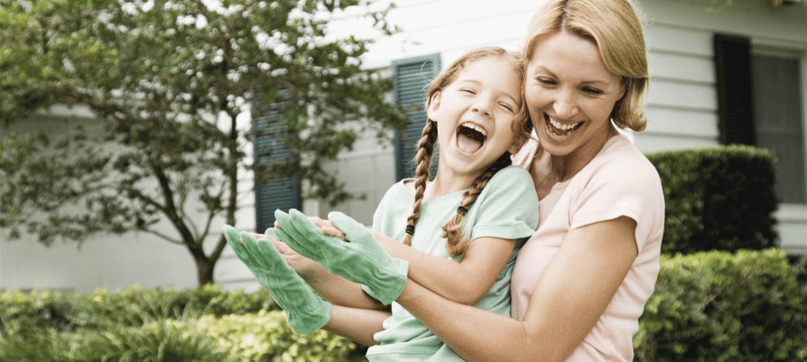 Mother and daughter laughing outdoors, the girl wearing green gloves.