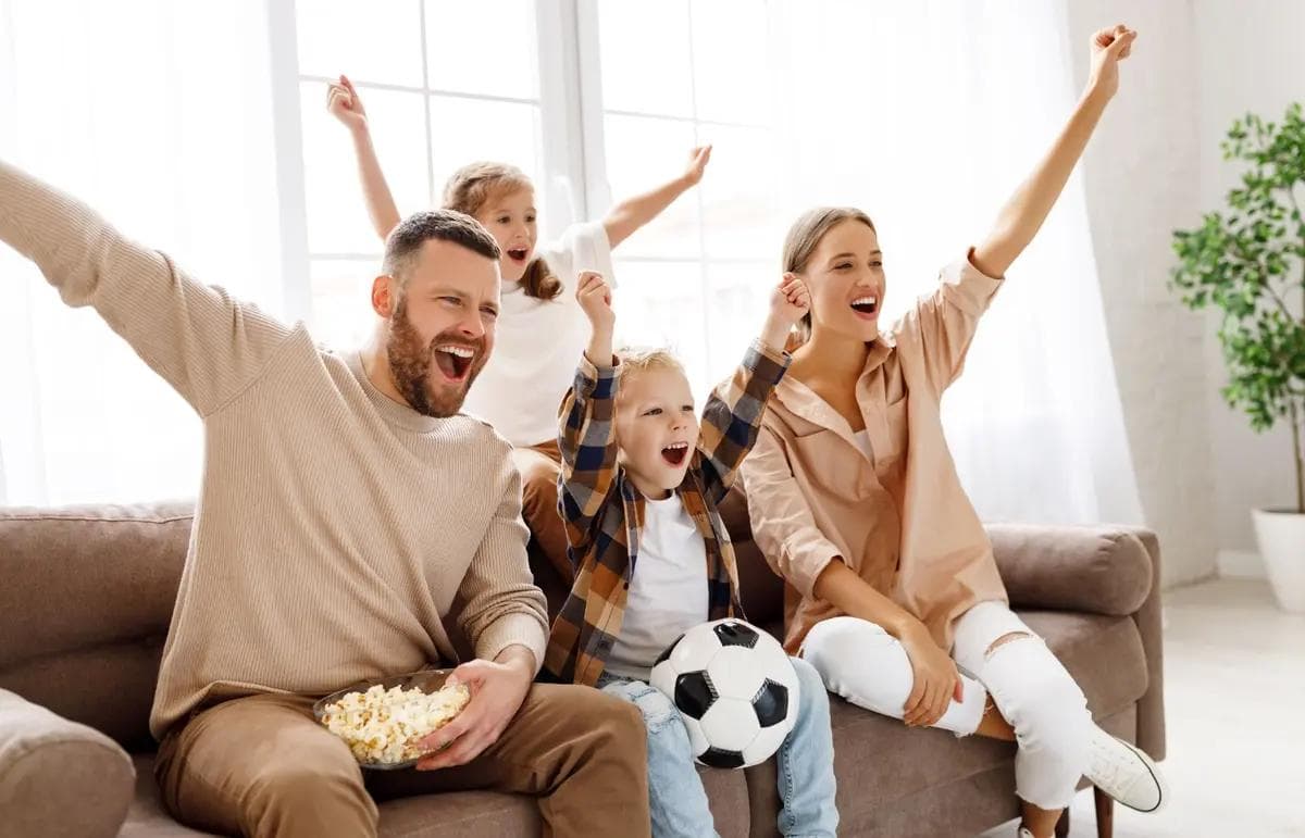 Eine Familie sitzt auf einem Sofa und schaut ein Fußballspiel an.