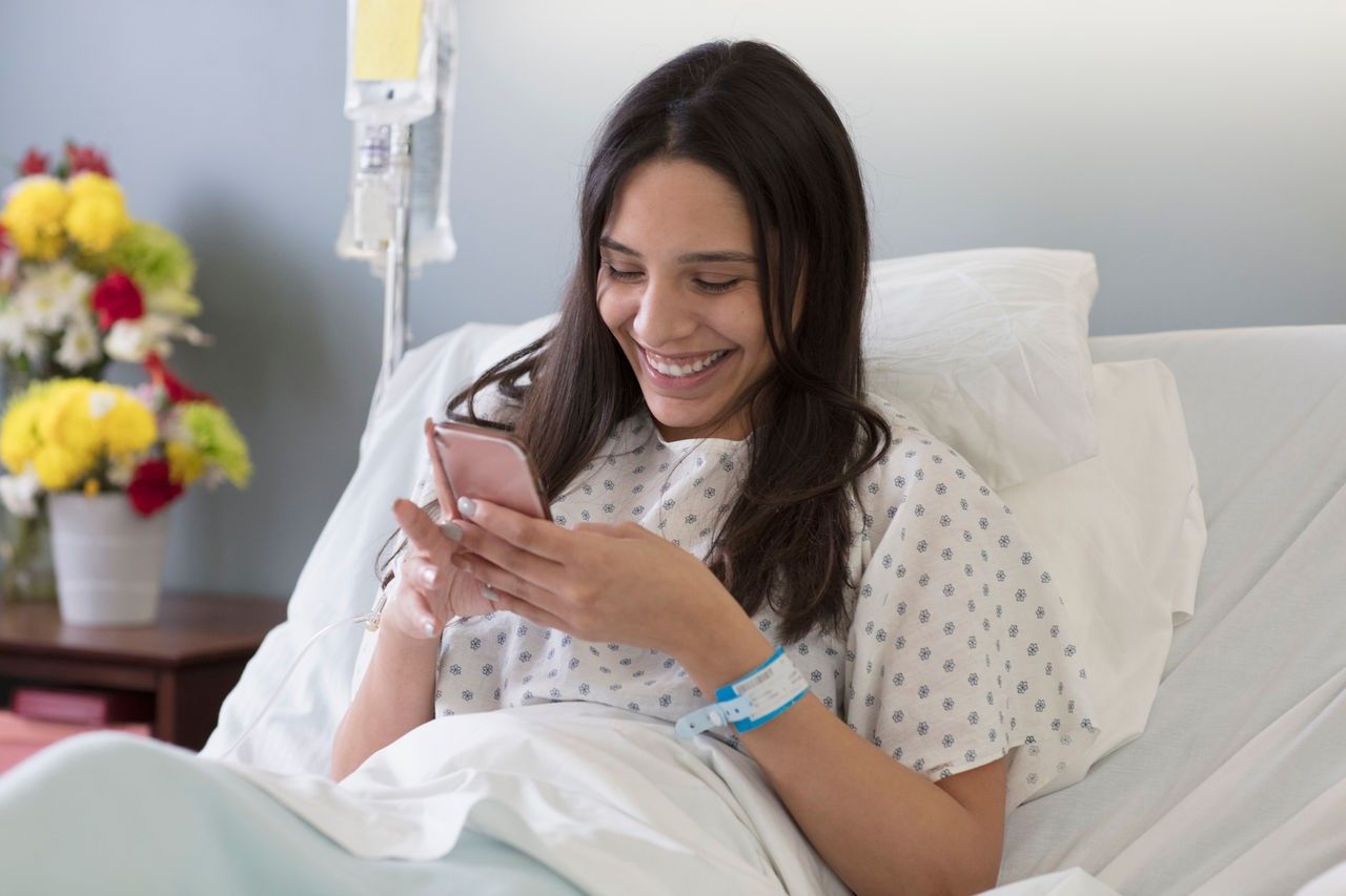 Eine Frau sitzt mit einem Laptop und Kopfhörern auf einem Bett.